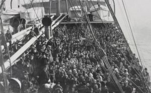A standing-room only crowd of immigrants on the deck of a steamship bound for the United States.