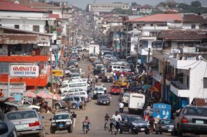 A crowded urban streetscape in Monrovia, Liberia, shows a lot of cars and small commercial buildings. 