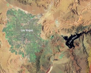 A satellite image shows a place in the Mojave Desert with Lake Mead in the east and the city of Las Vegas -- some of which is green -- to the west. Both the lake and the city are surrounded by brown. 