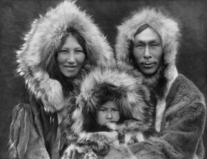 A married Inuit couple and their child, all bundled up wearing parkas. 