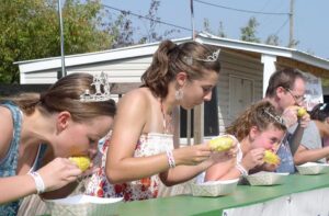 Three young ladies and a young man sit at an outdoor table an eat corn on the cob.