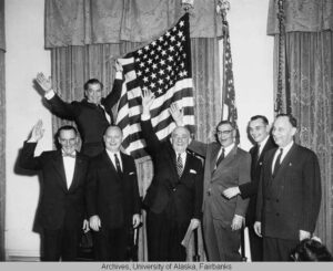 A black and white photo taken in 1959 that shows Alaska officials celebrating and waving beside an American flag that has 49 stars.