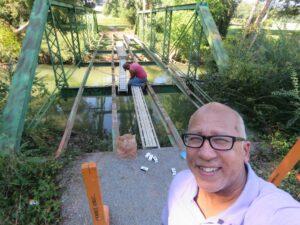 Calvin Sneed stands in front of a steel truss bridge while someone is repairing it. 