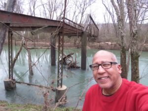 Calvin Sneed stands in front of a bridge that has fallen apart. 